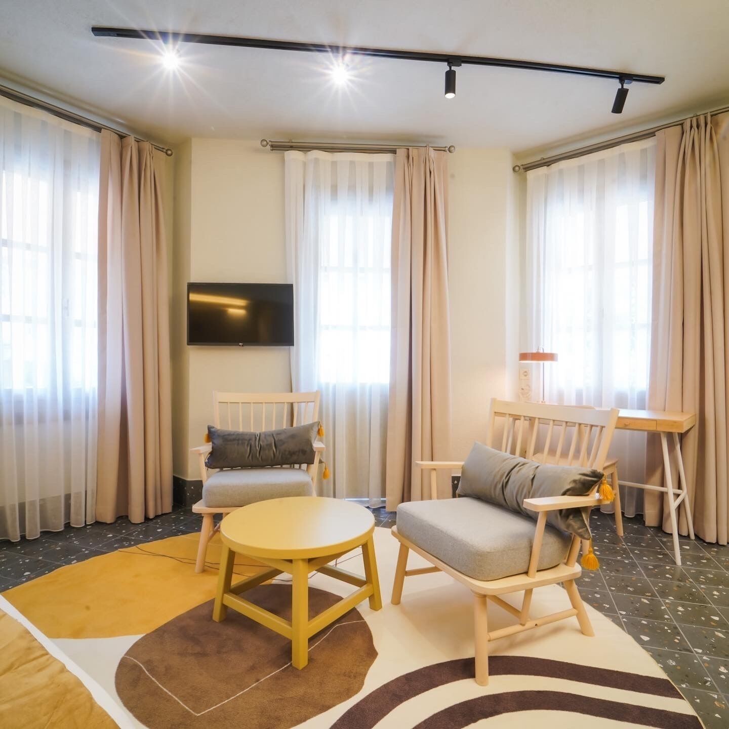 A modern living room with a flat-screen TV, two wooden chairs, a small round table, and a coffee table.