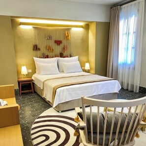 A hotel room with a large bed, two bedside lamps, a small table with a chair, a decorative wall hanging, and a view of the outside through sheer curtains. - Bono Hotel Old Town (Marmaris)