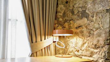 A wooden desk with a chair, a lamp, and a stone wall.