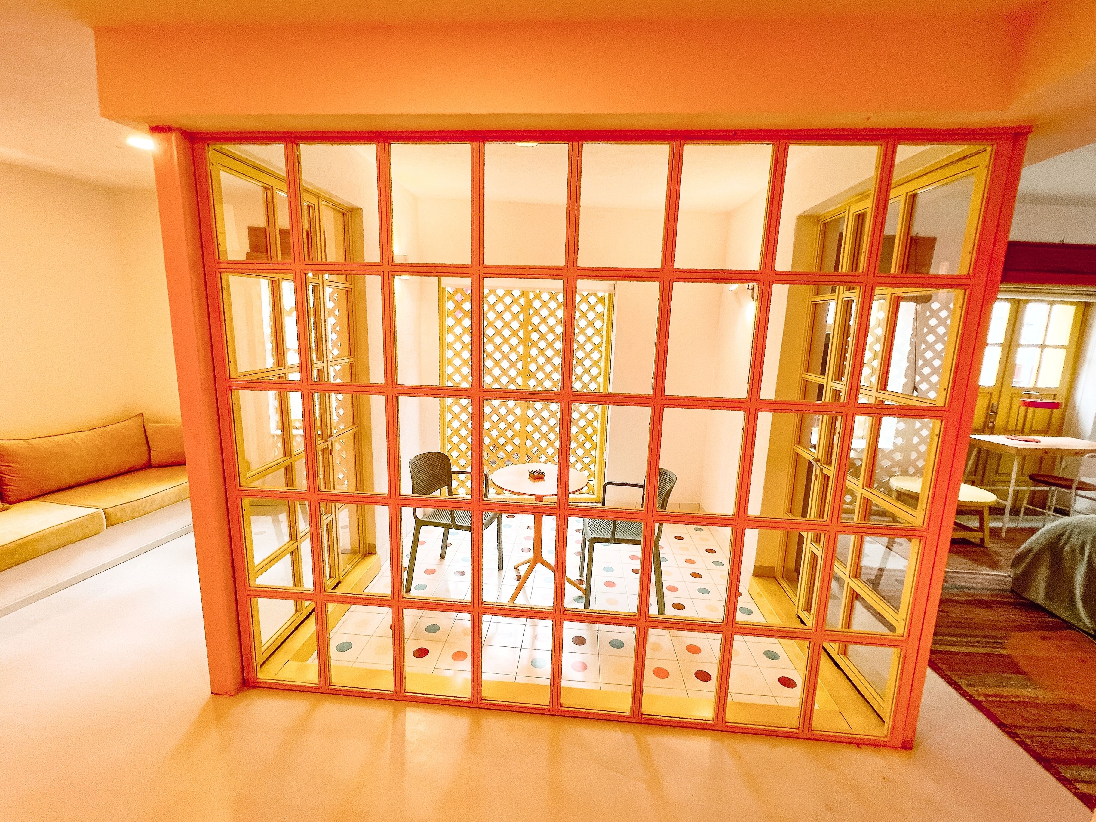 A room with a partition featuring a grid of glass panels, a round table with chairs, and a patterned floor.