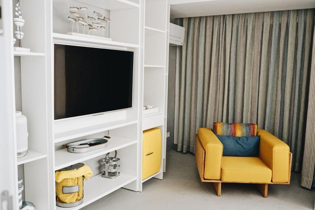 Un salón moderno con un televisor de pantalla plana, un sofá amarillo y una cortina a rayas.