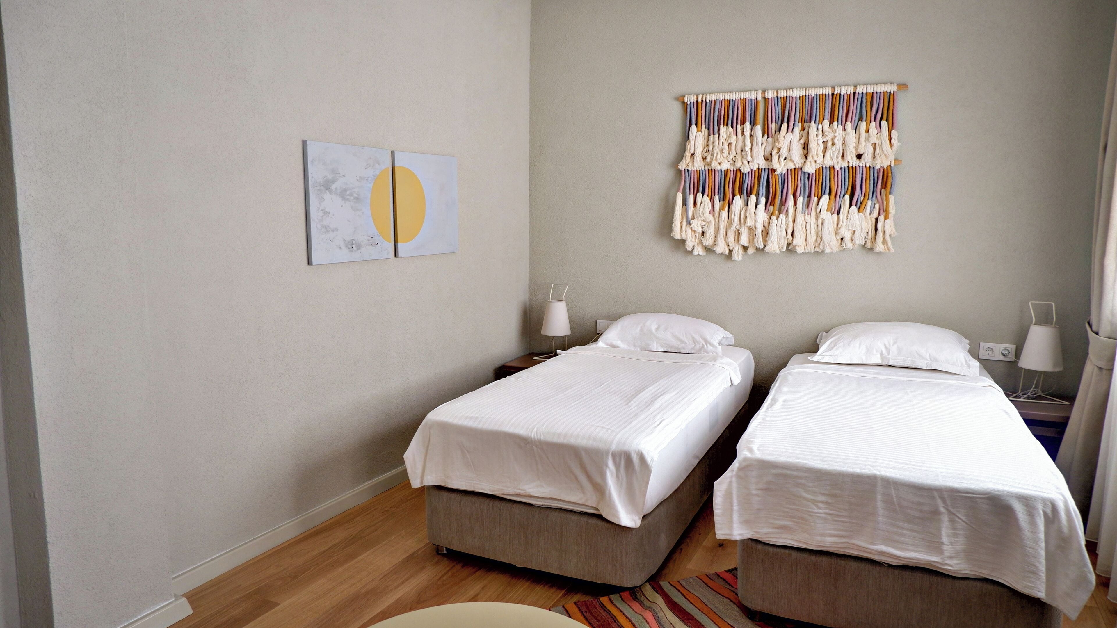 Habitación de hotel con dos camas individuales, una paleta de colores neutros y un adorno decorativo en la pared.