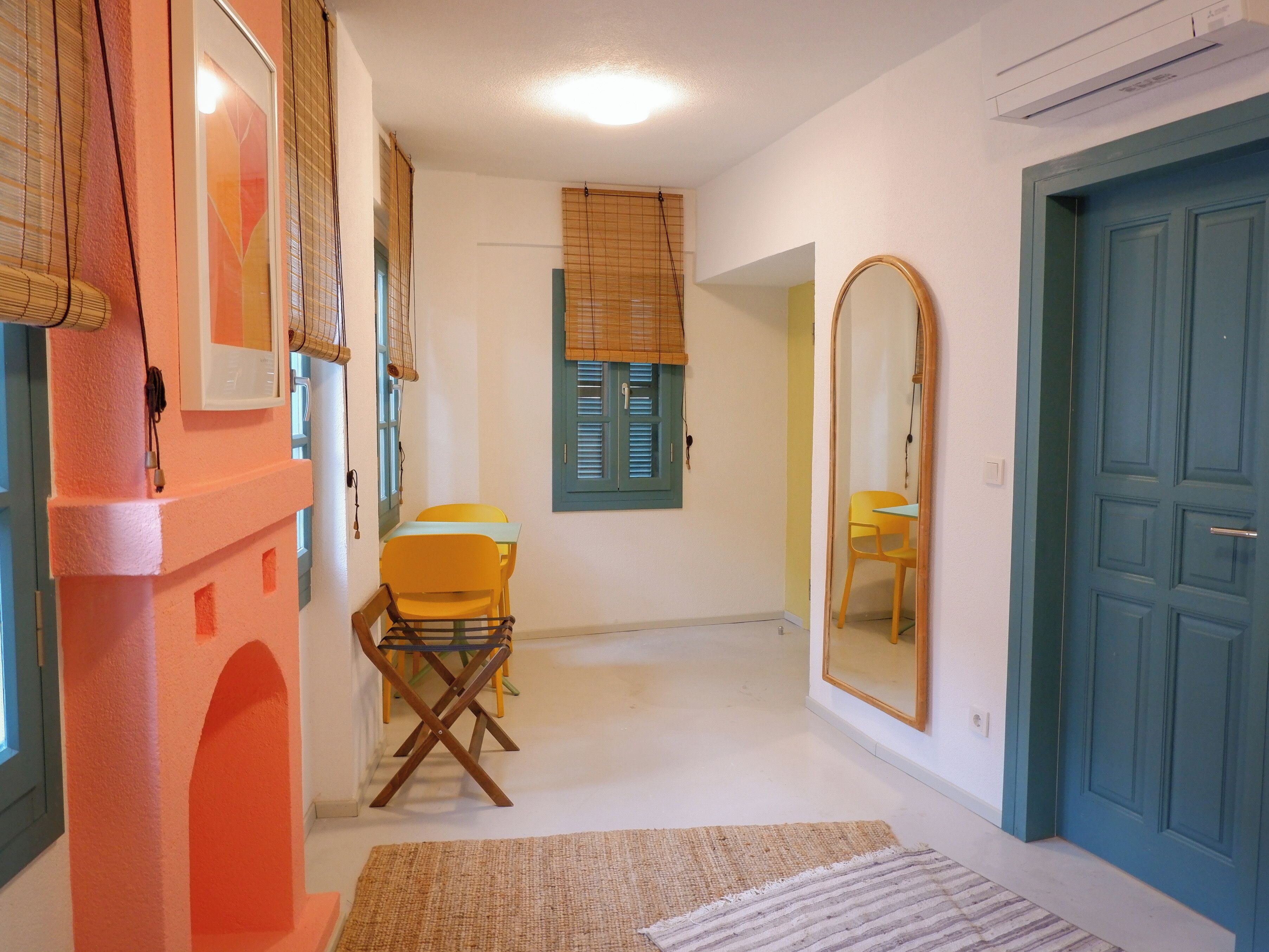A narrow hallway with a small table and chairs, a mirror, and a blue door.
