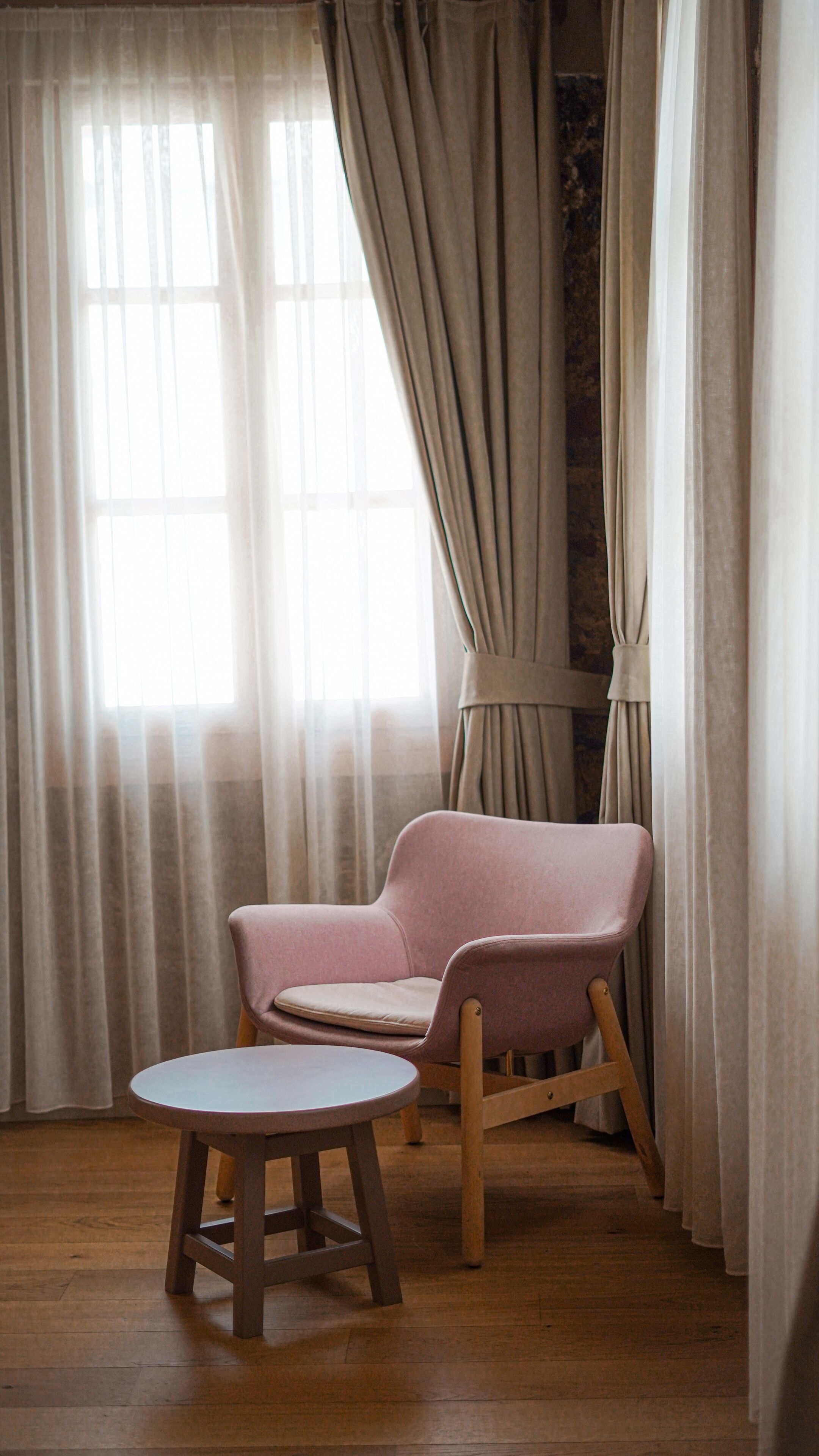 A room with a wooden floor, a pink armchair, and a small round table.