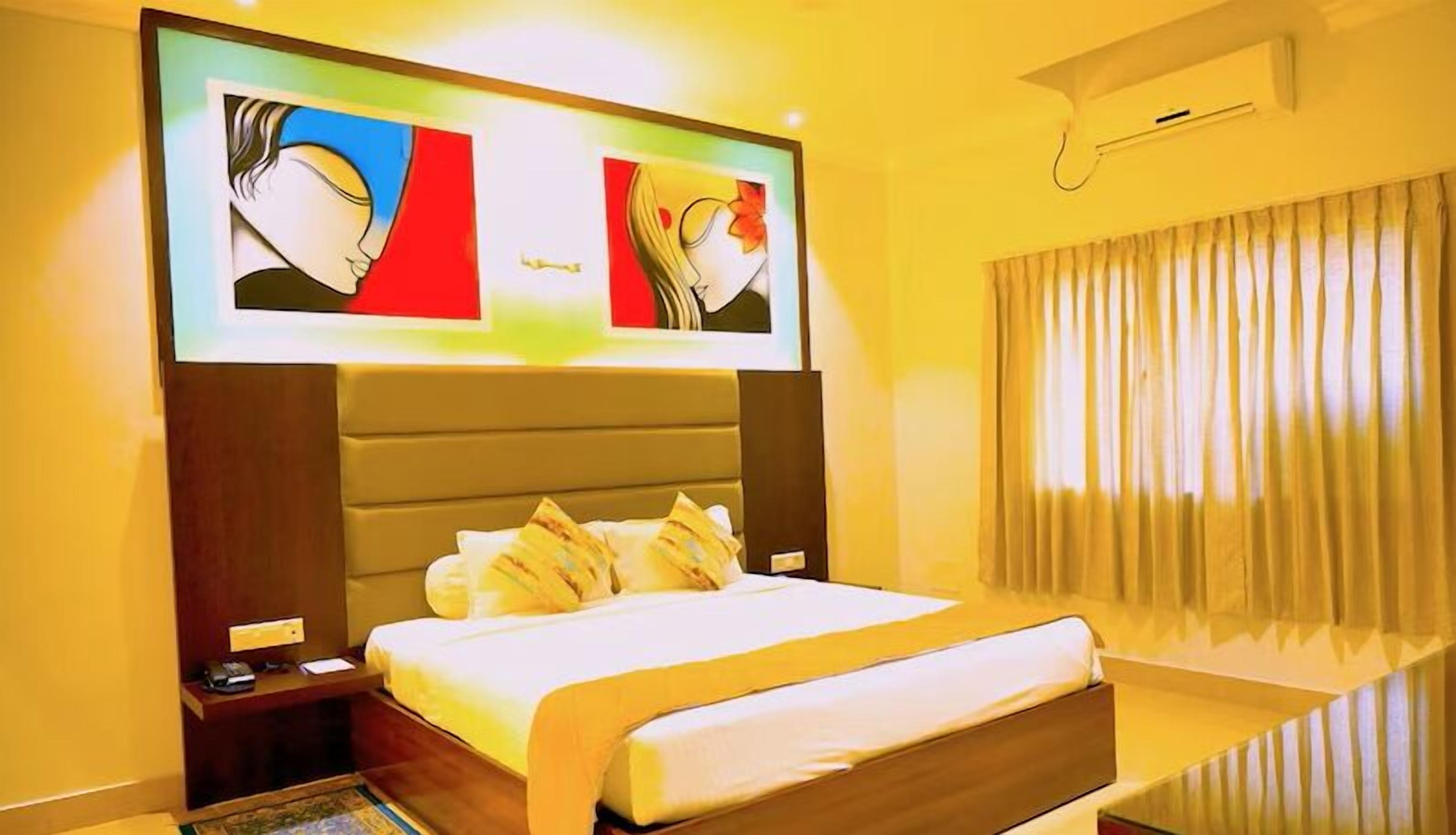 A hotel room with a large bed, a nightstand, a TV mounted on the wall, and a window with curtains.