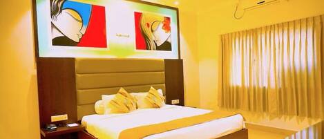 A hotel room with a large bed, a nightstand, a TV mounted on the wall, and a window with curtains.