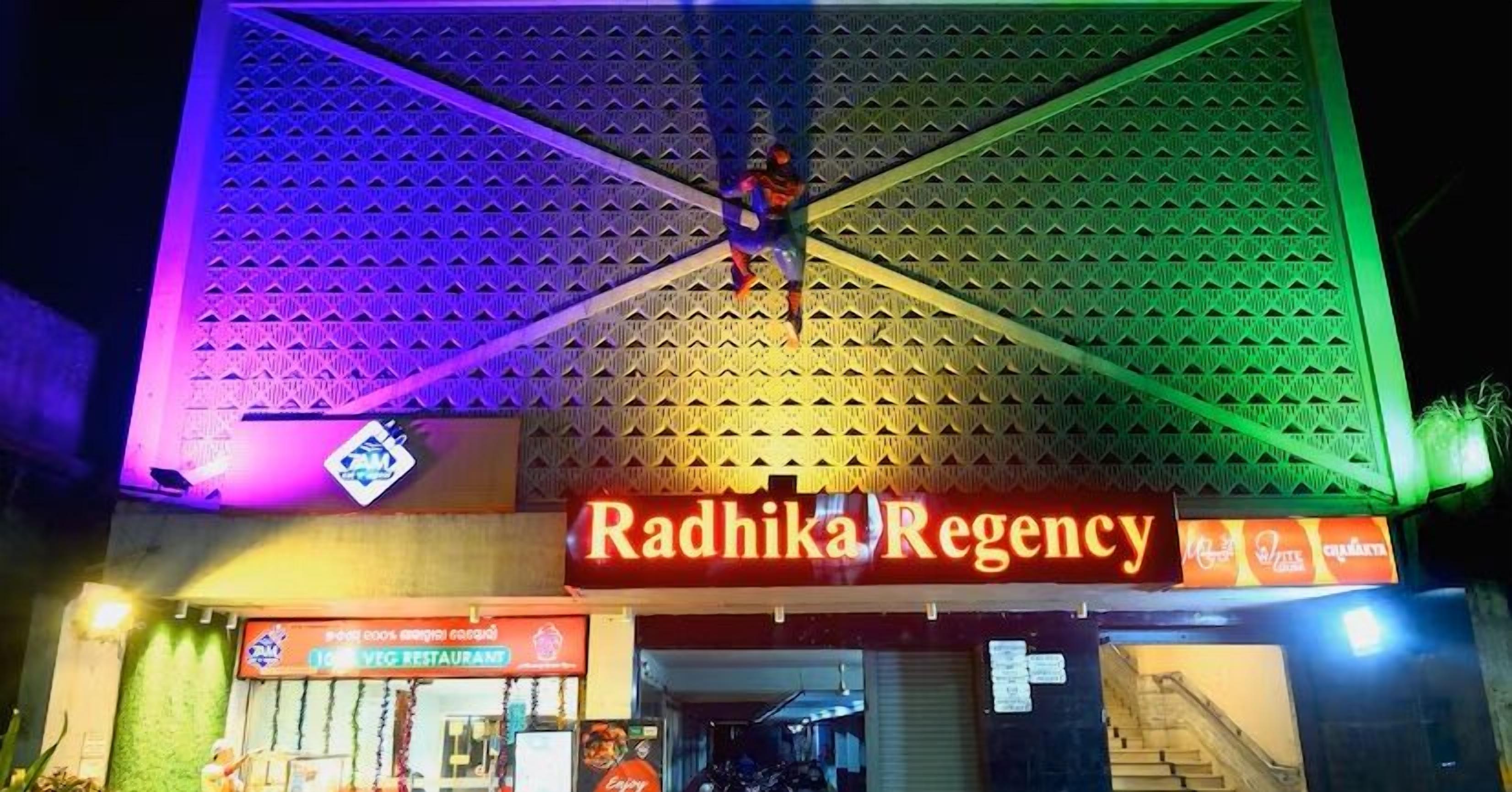 A building with a sign reading "Radhika Regency" and a vegetarian restaurant sign below it.