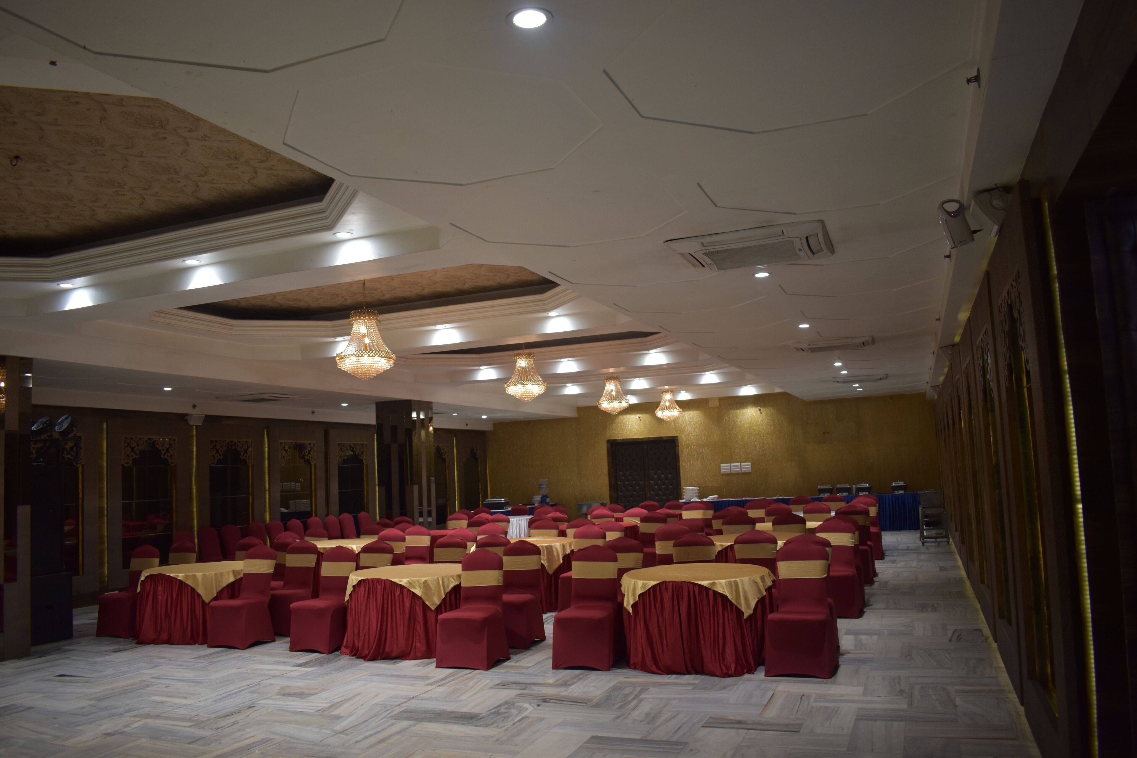 Un salón de banquetes con filas de sillas y mesas rojas, un techo alto con iluminación empotrada y un piso de mármol.