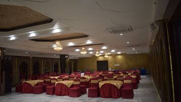 Un salón de banquetes con filas de sillas y mesas rojas, un techo alto con iluminación empotrada y un piso de mármol.