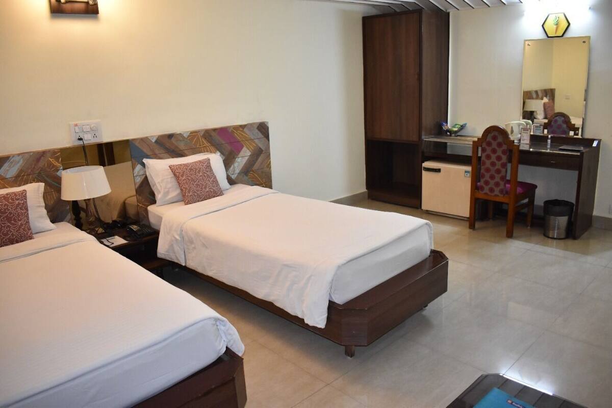 Habitación de hotel con dos camas, un escritorio, una silla, un espejo y un mueble auxiliar.
