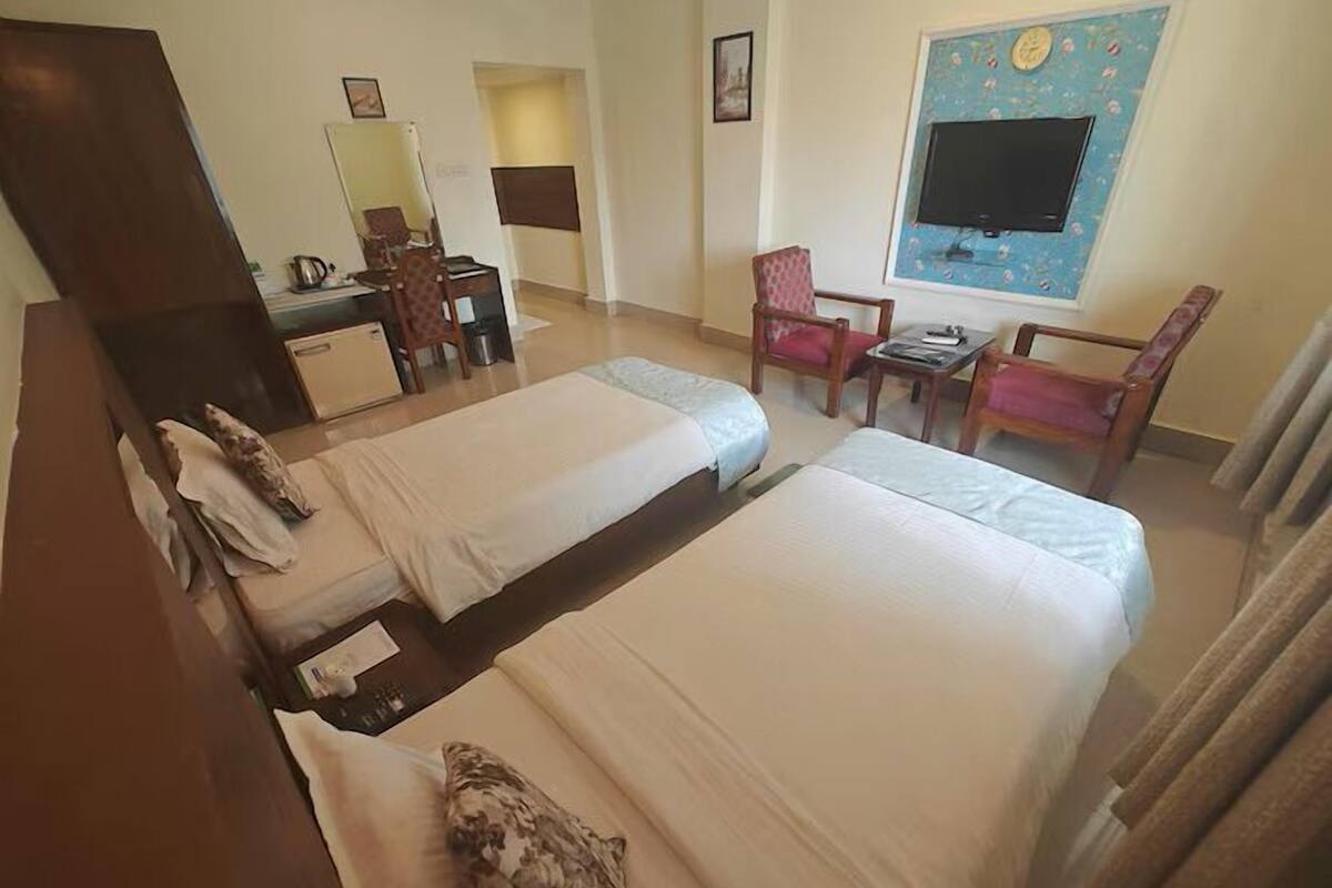Habitación de hotel con dos camas, un escritorio, una silla, un televisor y un cuadro en la pared.