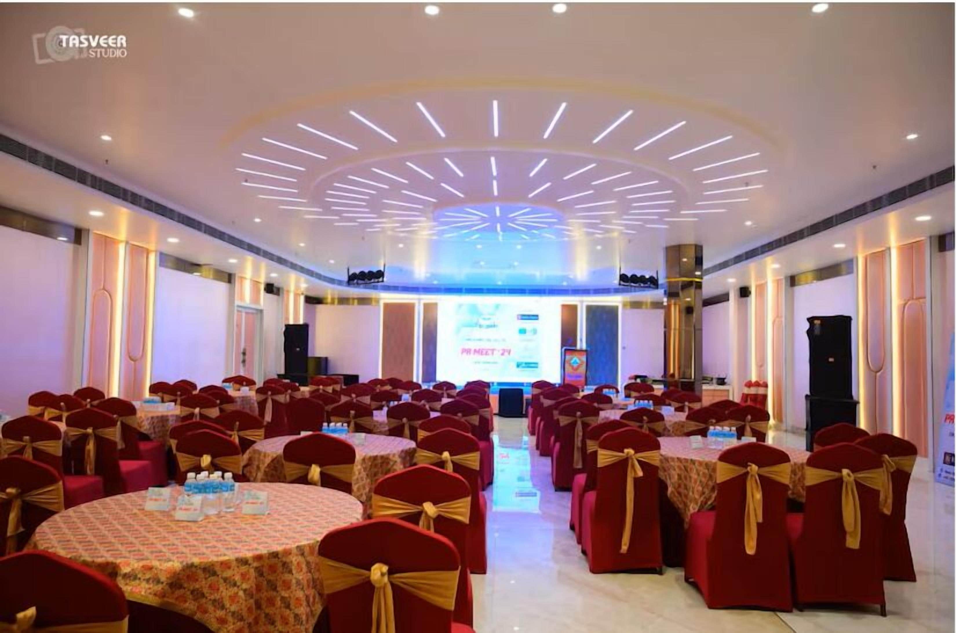 A conference room with round tables, red chairs with gold sashes, and a large screen at the front.