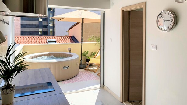 A modern bathroom with a bathtub, a sink, and a shower area. There is a clock on the wall and a view of the outside balcony. - Apartment Shiny Love (Split)