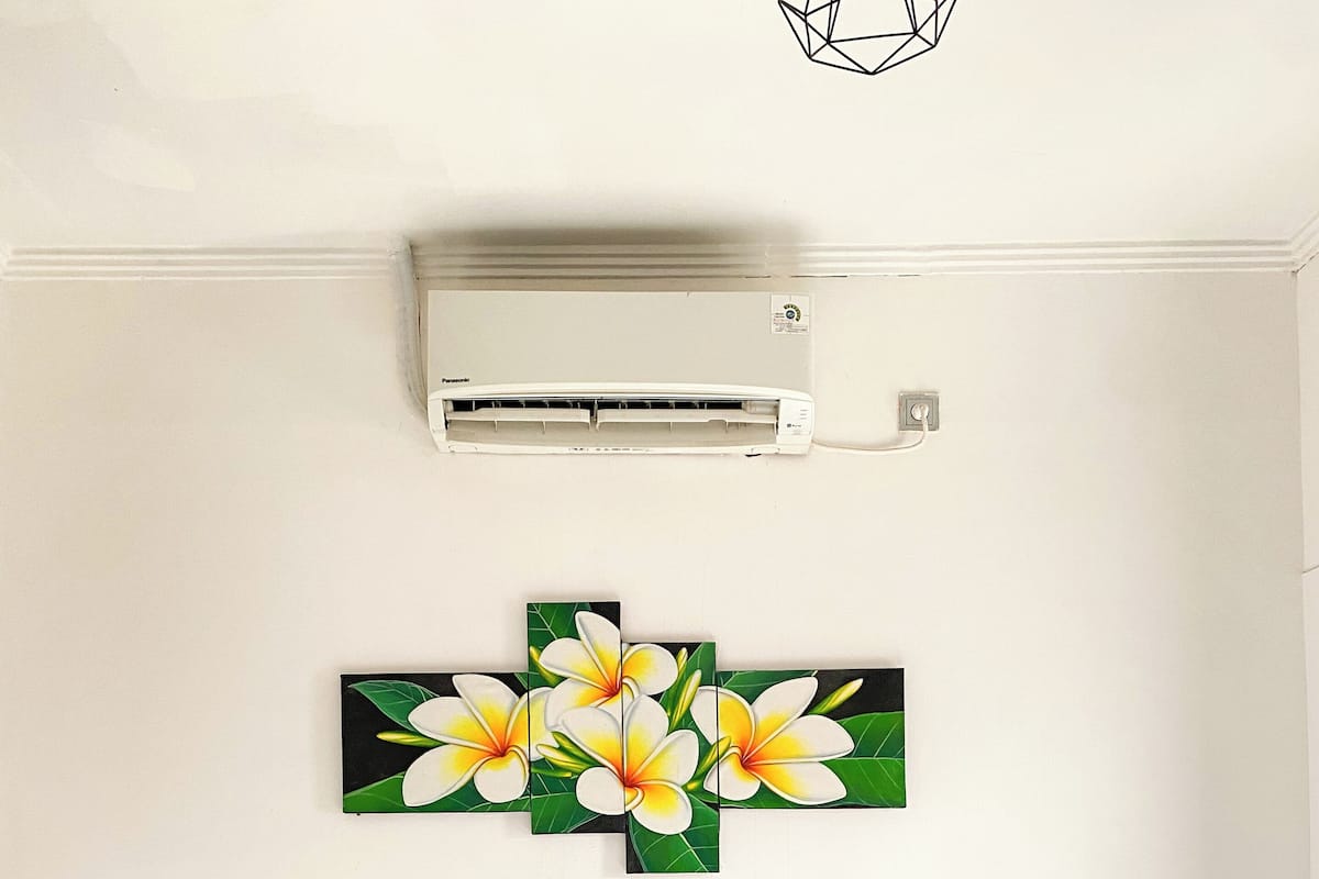 Un dormitorio con cama, ropa de cama blanca, cabecera gris y aire acondicionado instalado en la pared.