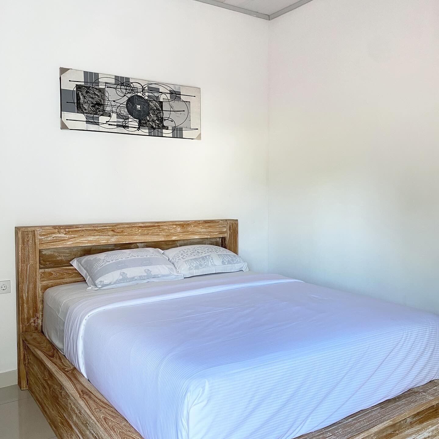 Une chambre avec un lit en bois, une literie blanche et une œuvre d’art abstraite accrochée au mur.