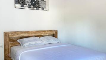 Une chambre avec un lit en bois, une literie blanche et une œuvre d’art abstraite accrochée au mur.