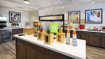 A breakfast bar with a sign that reads "HAPPY BREAKFAST STARTS HERE," a coffee machine, a fruit display, and a refrigerated display case.