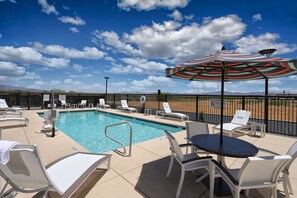 A poolside area with lounge chairs, a table, and an umbrella. - Hampton Inn & Suites Tucson Tech Park (Tucson)