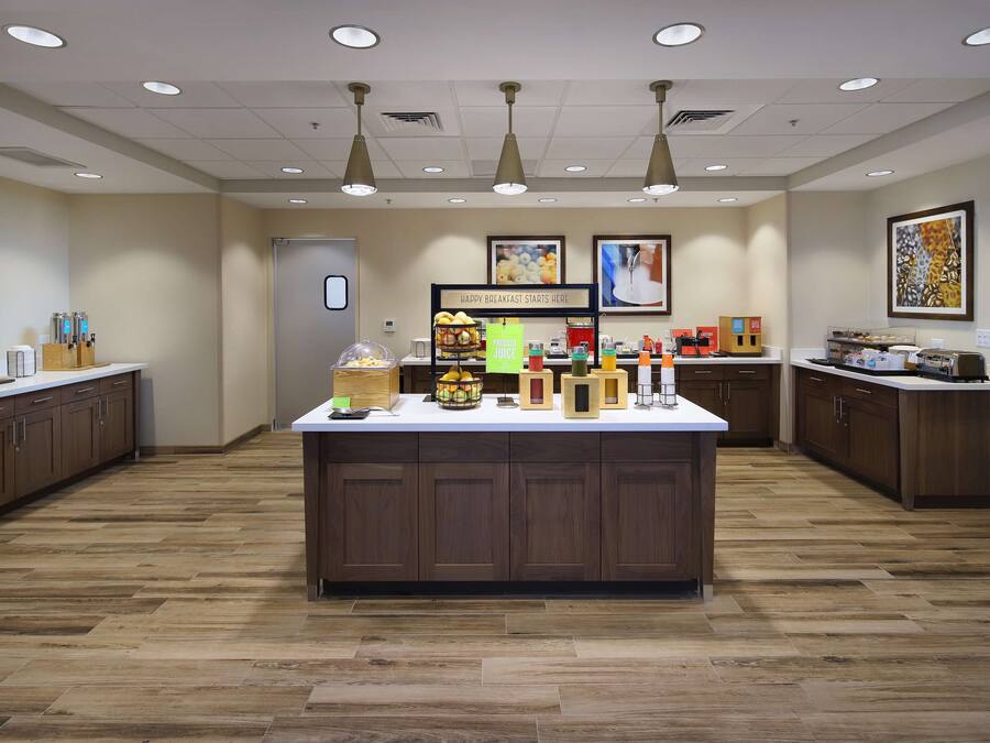 A modern kitchen with a central island, wooden cabinets, and a variety of breakfast items.