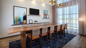 A modern hotel dining area with a long wooden table, cushioned chairs, a flat-screen TV, and artwork on the walls. - Hampton Inn & Suites Tucson Tech Park (Tucson)