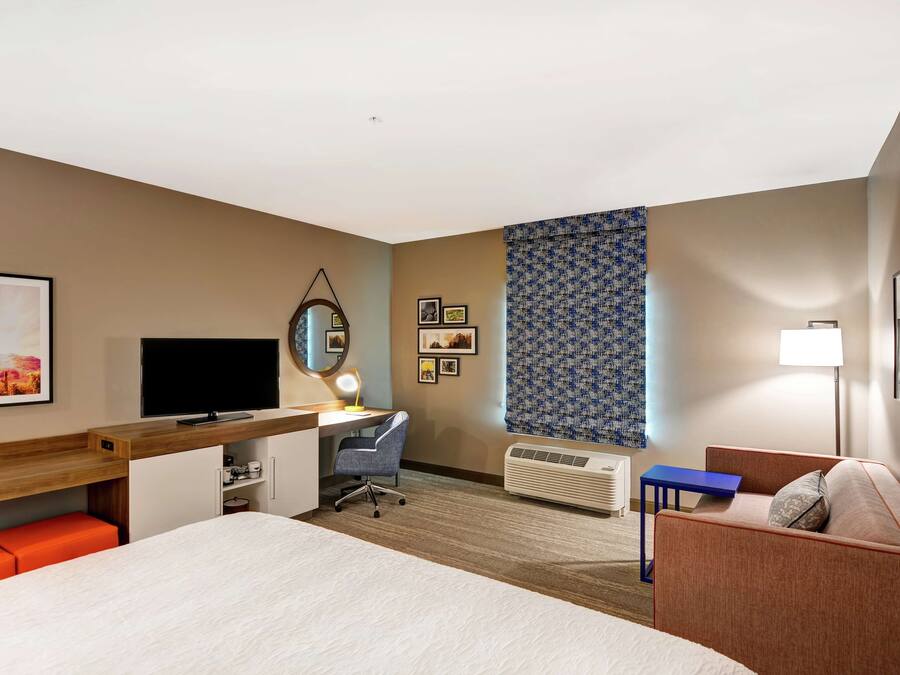 A hotel room with a bed, desk, chair, TV, and a small table.