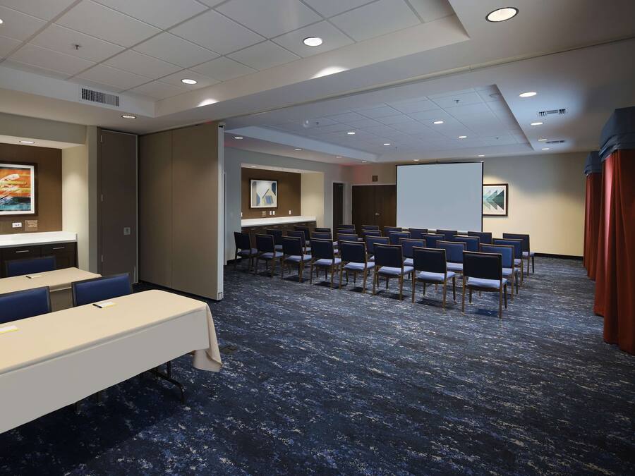 A conference room with a long table, rows of chairs, a projector screen, and a presentation screen.