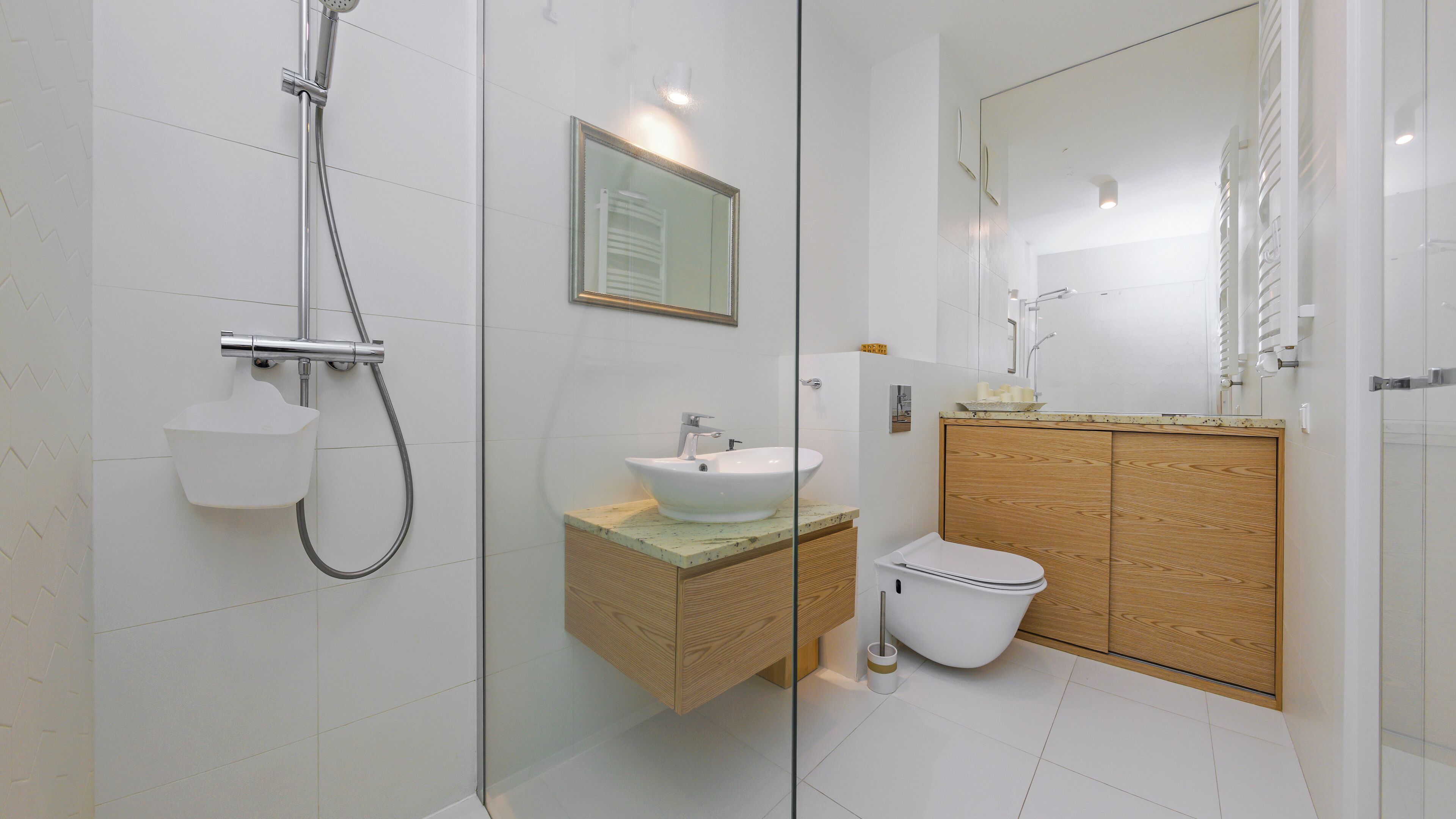 Un baño moderno con ducha de vidrio, lavamanos blanco y tocador de madera.