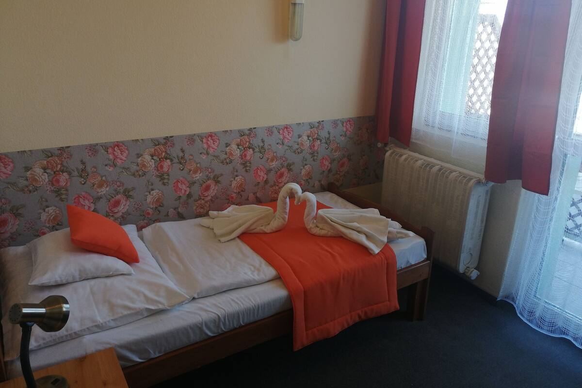 A single bed with a floral headboard, a red blanket, and a pillow.