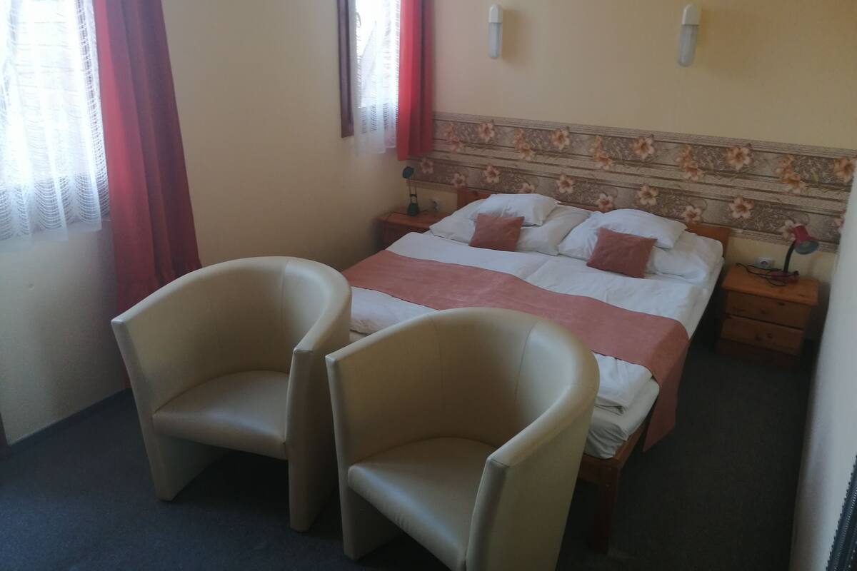 A hotel room with a bed, two armchairs, a nightstand, and a wall-mounted lamp.
