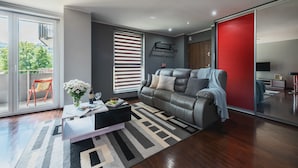 Een moderne woonkamer met een grijze bank, een bijzettafeltje en een groot raam met jaloezieën.