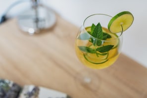 Een glashelder glas met een stukje limoen en muntblaadjes, mogelijk een cocktail, op een houten ondergrond.