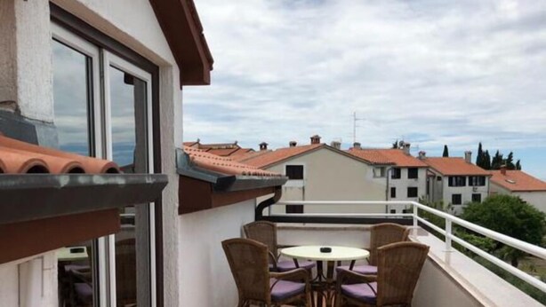 A balcony with a table and chairs, a sliding glass door, and a view of neighboring buildings. - Apartments Adriana (Tar-Vabriga)