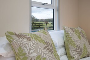 A bedroom with a large window, a bed with white linens, and two pillows with a leaf pattern.