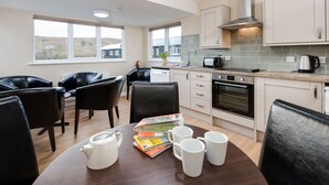 A modern kitchen with white cabinets, a built-in oven, and a dining area with a wooden table and black chairs. - Brown Rigg Guest Rooms (Hexham)