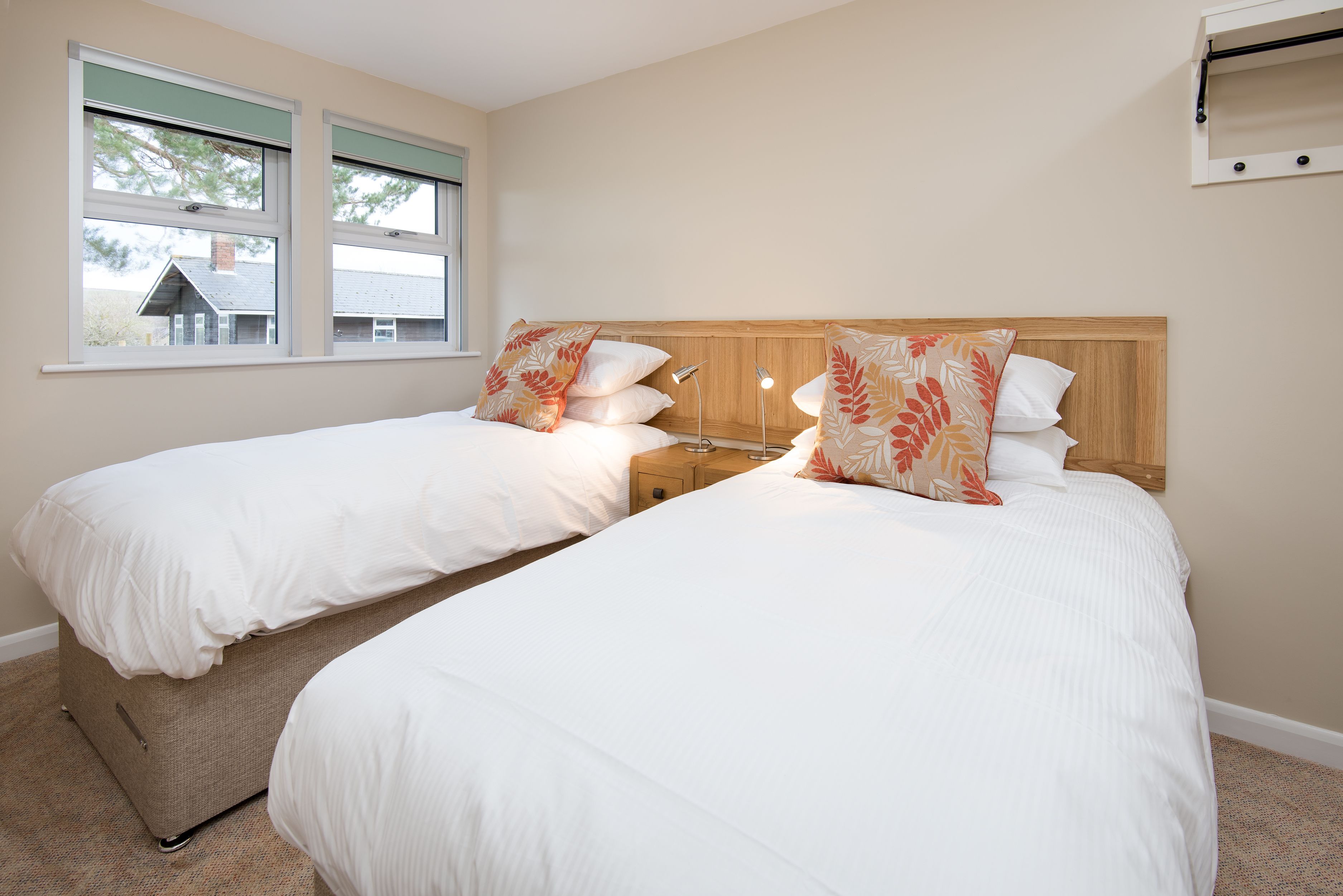 Een hotelkamer met twee bedden, een houten hoofdeinde, een nachtkastje en een raam met uitzicht op een huis.