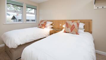 Een hotelkamer met twee bedden, een houten hoofdeinde, een nachtkastje en een raam met uitzicht op een huis.