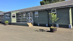 A single-story building with a green exterior, a front porch with steps, and a small tree in a planter. - Brown Rigg Guest Rooms (Hexham)