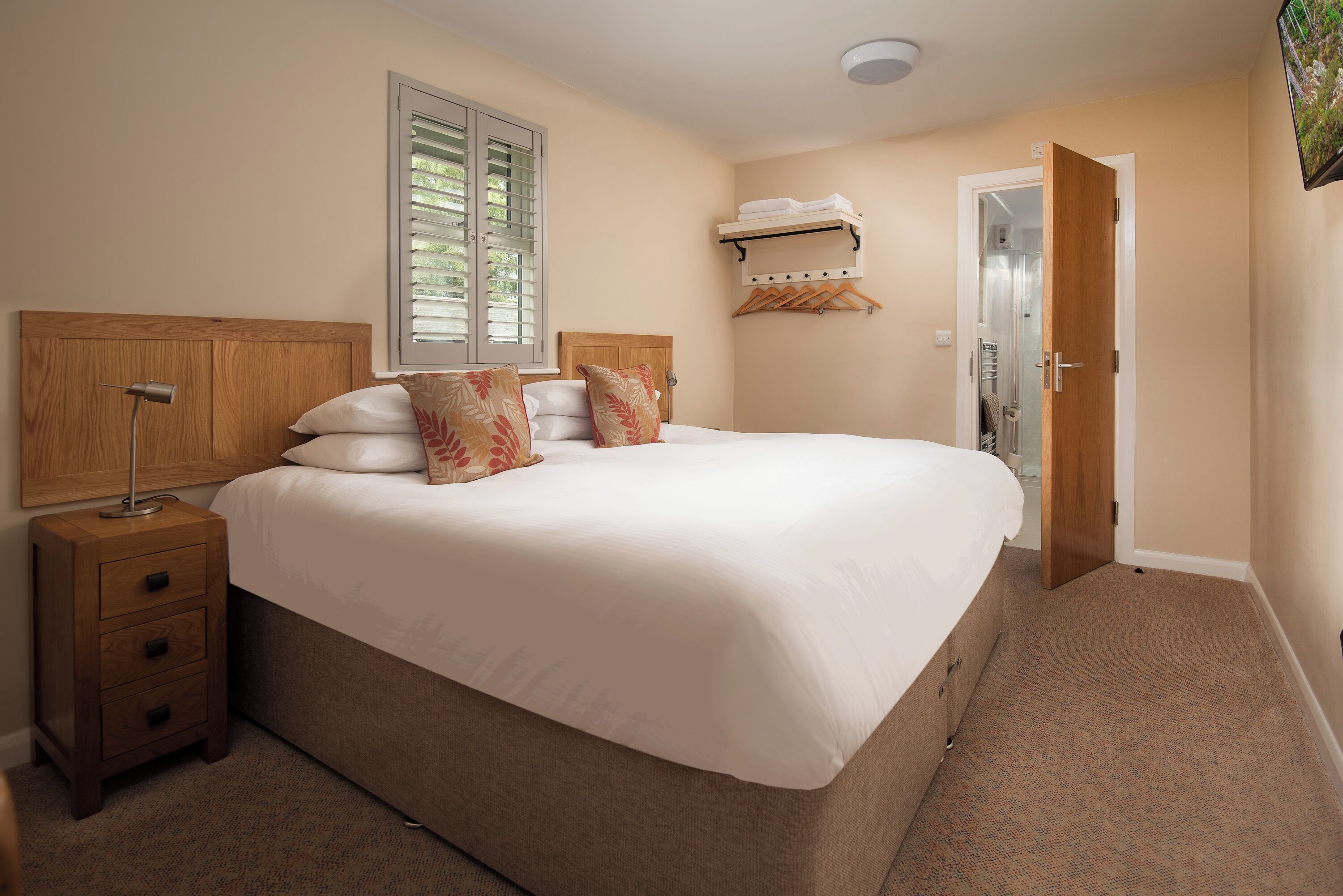 A bedroom with a large bed, wooden headboard, bedside tables, a window with blinds, a coat rack, and a door.