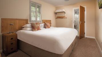 A bedroom with a large bed, wooden headboard, bedside tables, a window with blinds, a coat rack, and a door.