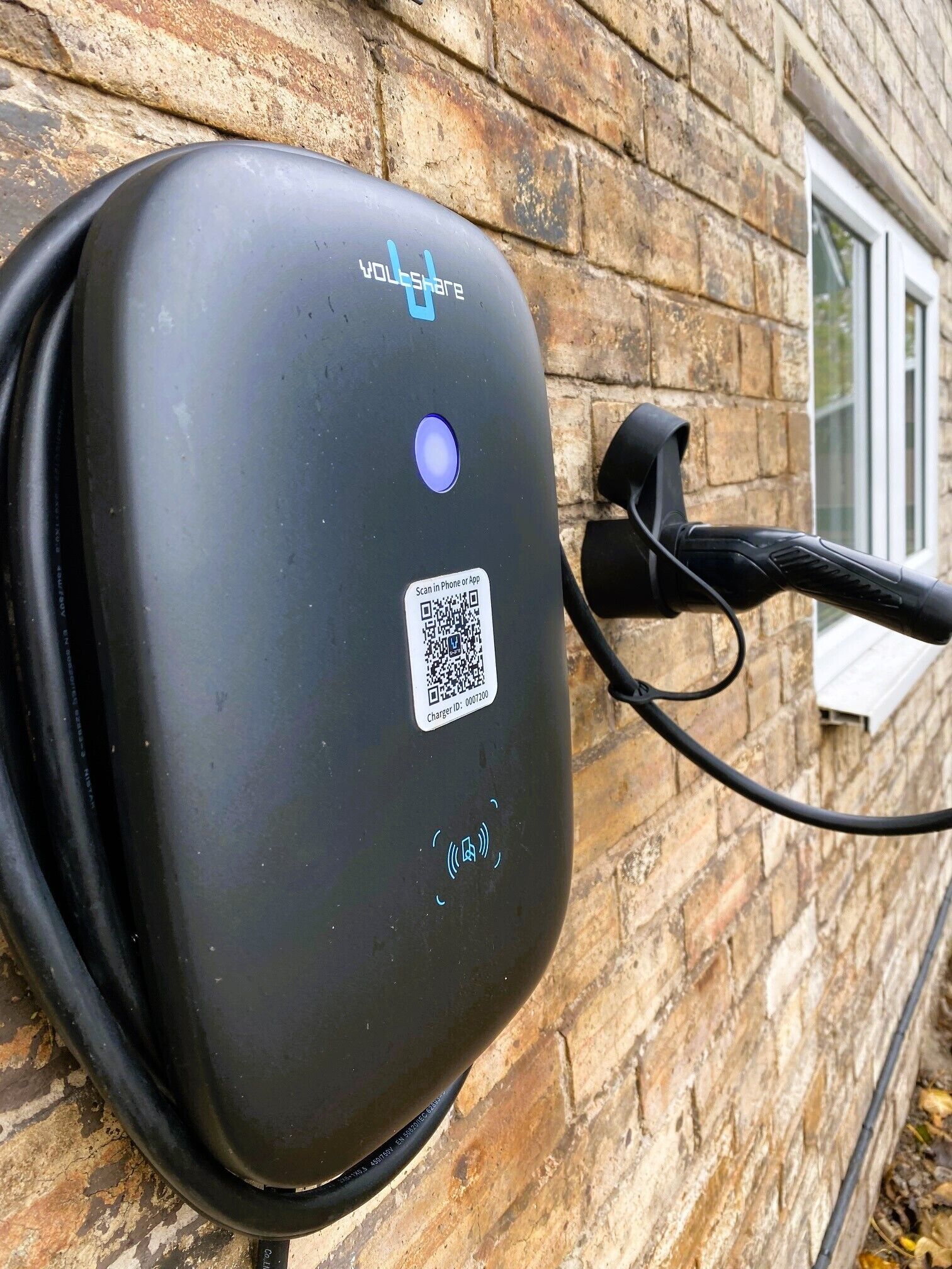 Una stazione di ricarica per veicoli elettrici nera fissata a un muro in mattoni.