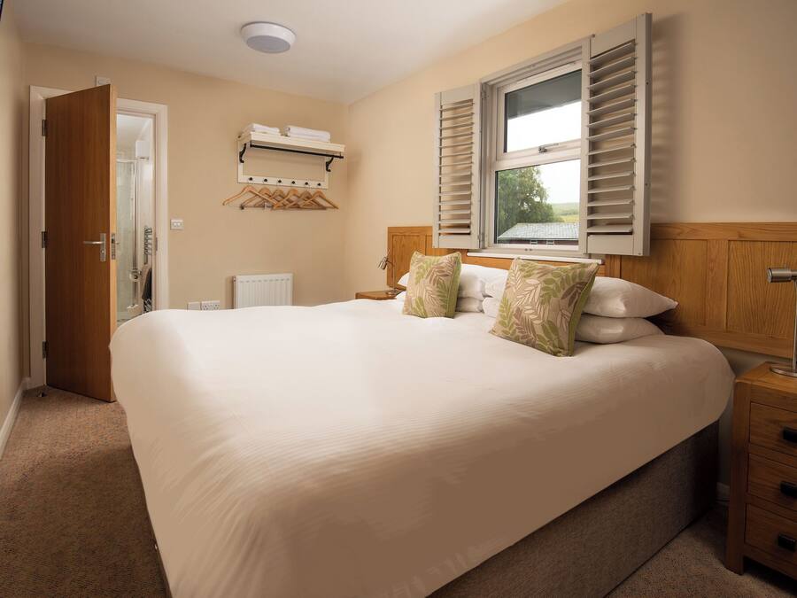 A bedroom with a large bed, a bedside table, a lamp, a window with shutters, and a wall-mounted heater.