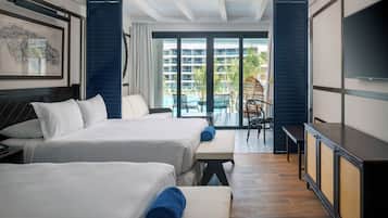A hotel room with two beds, a TV, a balcony with a view of the pool and buildings, and a dining area with chairs.