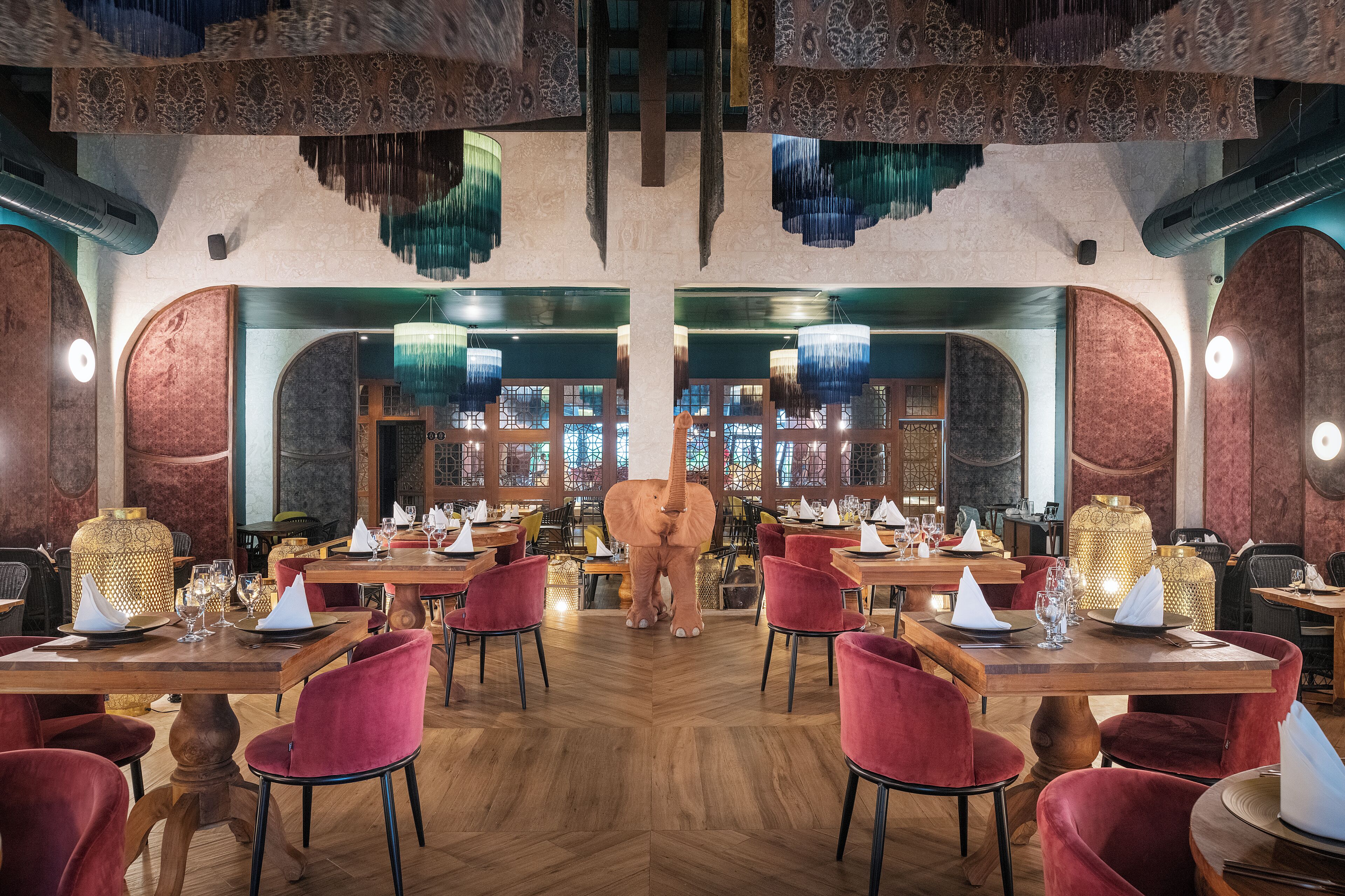 Un restaurante con mesas de madera, sillas rojas y una gran estatua de elefante en el centro.