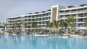 A modern hotel with a large swimming pool, multiple balconies, and sun loungers.