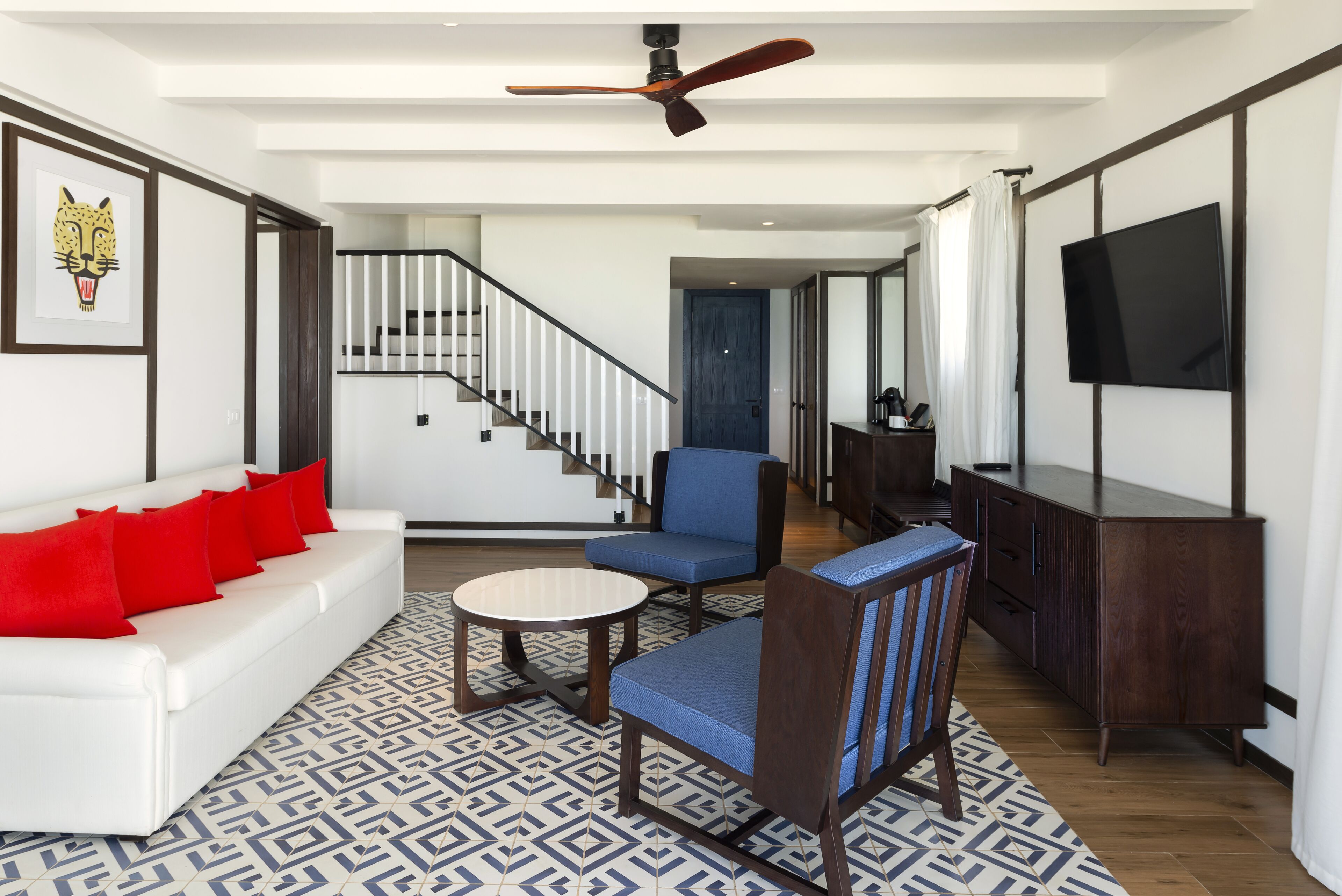 A modern living room with a white sofa, red cushions, a blue armchair, a coffee table, and a TV on the wall.