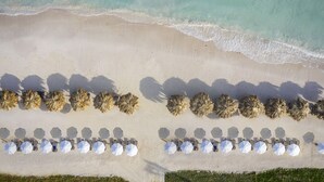 Vista aérea de uma praia com fileiras de espreguiçadeiras e guarda-sóis, e uma visão clara do oceano.