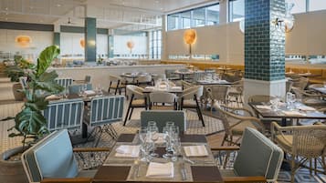 Ein geräumiges Restaurant mit hohen Decken, großen Fenstern und unterschiedlichen Sitzgelegenheiten, darunter Tische und Stühle.