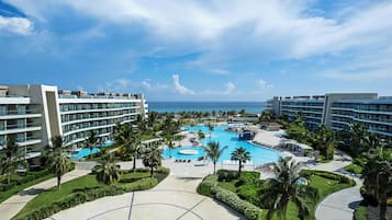 A resort with a central pool, multiple buildings, and a clear view of the ocean.