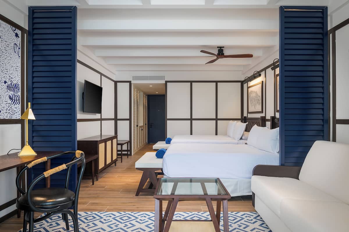 Habitación de hotel con dos camas, un escritorio, una silla, un televisor y un ventilador de techo.