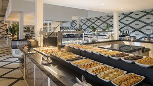 A buffet with various food items, a tiled floor, and a modern kitchen area in the background.
